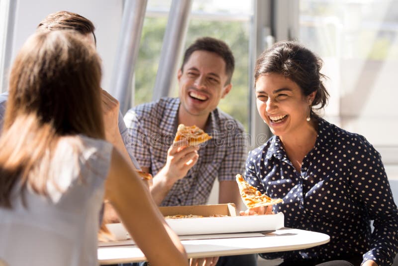 Indian woman laughing, eating pizza with colleagues in office