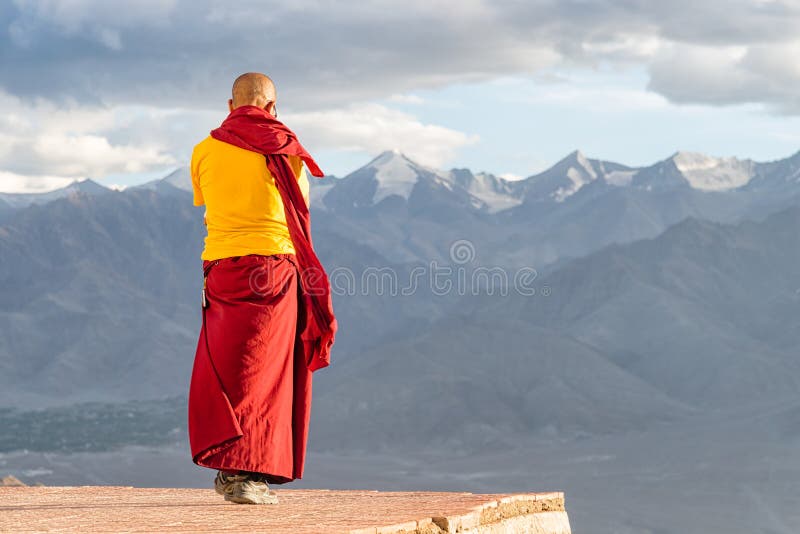 Indian tibetan monk lama in red and yellow color clothing standing in front of mountains - with copy space on right side for design or text. Indian tibetan monk lama in red and yellow color clothing standing in front of mountains - with copy space on right side for design or text