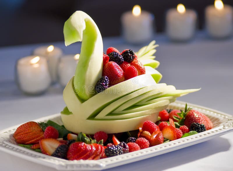 A decorative fresh fruit display with a honeydew melon carved in the shape of a swan surrounded with sliced fruit. A decorative fresh fruit display with a honeydew melon carved in the shape of a swan surrounded with sliced fruit.