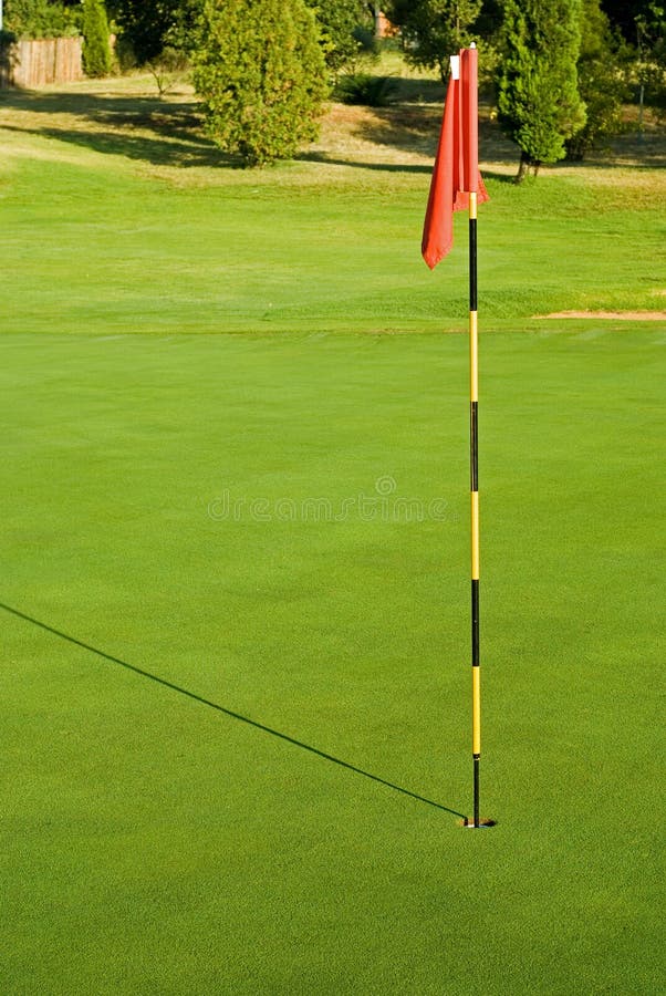 Striped golf flag in green hole with morning shadow on grass. Striped golf flag in green hole with morning shadow on grass