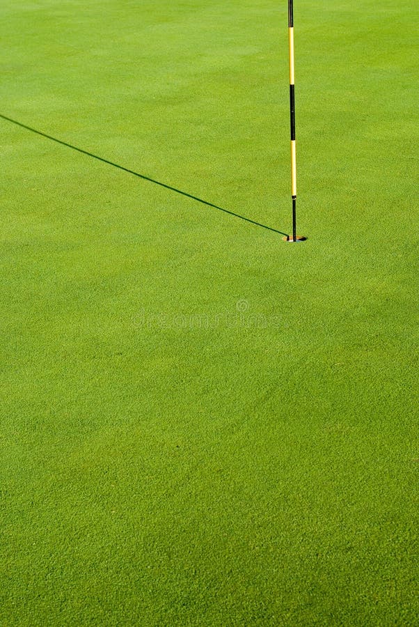 Striped golf flag in green hole with morning shadow on grass. Striped golf flag in green hole with morning shadow on grass