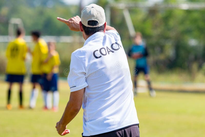Indietro dell'ALLENATORE bianco d'uso camicia dell'allenatore di football americano ad un campo di sport all'aperto che prepara i immagini stock libere da diritti Indietro dell'ALLENATORE bianco d'uso camicia dell'allenatore di football americano ad un campo di sport all'aperto che prepara i immagini stock libere da diritti