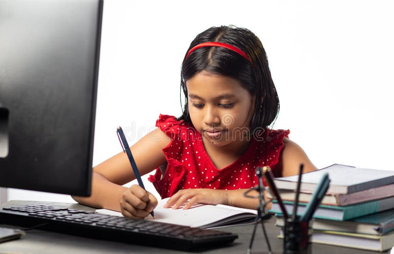 Indische Kindererziehung. Ein ziemlich schönes indisches Mädchen, das mit einem Desktop-Computer am Lerntisch auf weißem Hintergrund lernt