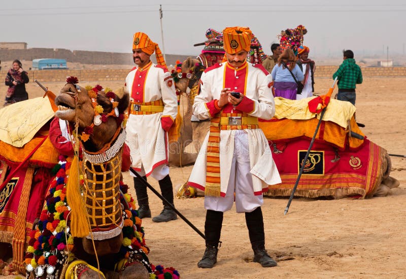 JAISALMER, INDIA: Indian man in old guardian uniform sending sms by mobile phone near camel of Desert Festival in Rajasthan. Every winter Jaisalmer takes the Desert Festival. JAISALMER, INDIA: Indian man in old guardian uniform sending sms by mobile phone near camel of Desert Festival in Rajasthan. Every winter Jaisalmer takes the Desert Festival