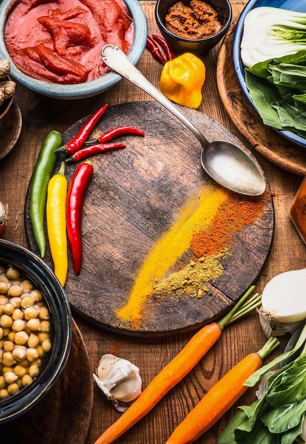 Indian vegetarian cooking ingredients with colorful ground spices , indian curry paste, chick peas , vegetables and spoon on wooden background, top view, frame. Healthy food and eating concept. Indian vegetarian cooking ingredients with colorful ground spices , indian curry paste, chick peas , vegetables and spoon on wooden background, top view, frame. Healthy food and eating concept