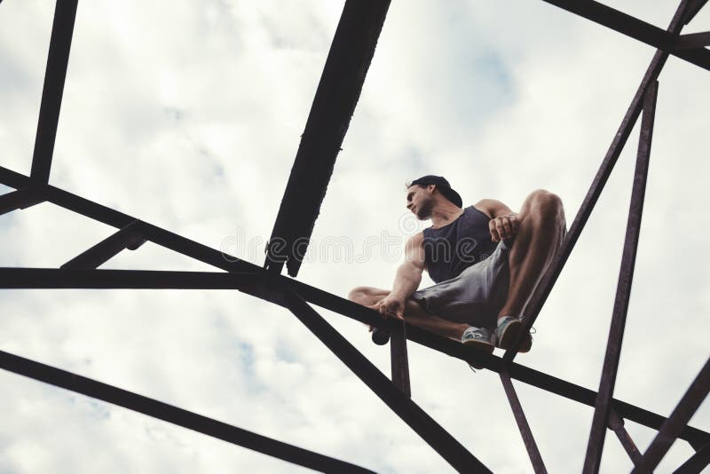 Individuo aventurado joven que equilibra y que se sienta en el top de alta construcción metálica fotos de archivo libres de regalías Individuo aventurado joven que equilibra y que se sienta en el top de alta construcción metálica fotos de archivo libres de regalías