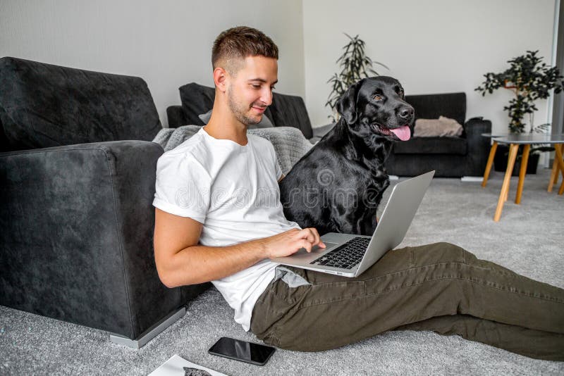 Individuo del Freelancer que sienta en casa el trabajo en ordenador portátil y con el perro adentro