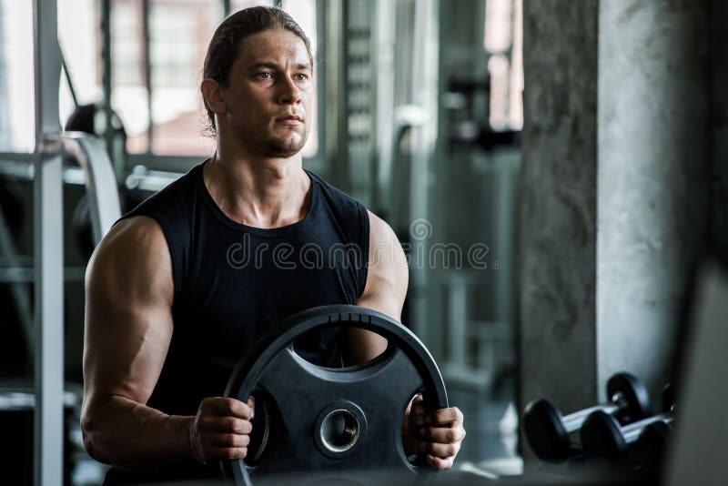 Individuo muscular del culturista que hace ejercicios con la placa del levantamiento de pesas en gimnasio entrenamiento joven del foto de archivo Individuo muscular del culturista que hace ejercicios con la placa del levantamiento de pesas en gimnasio entrenamiento joven del foto de archivo