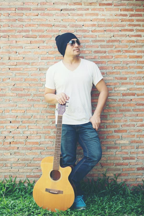 Indivíduo considerável que está mantendo a guitarra contra o posi da parede de tijolo imagem de stock Indivíduo considerável que está mantendo a guitarra contra o posi da parede de tijolo imagem de stock