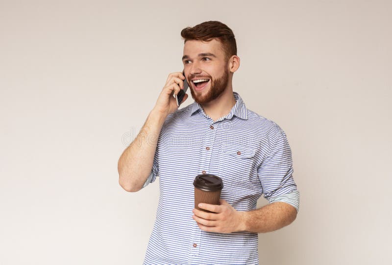 Indivíduo milenar considerável que fala no telefone celular e que guarda o café para ir fotos de stock Indivíduo milenar considerável que fala no telefone celular e que guarda o café para ir fotos de stock