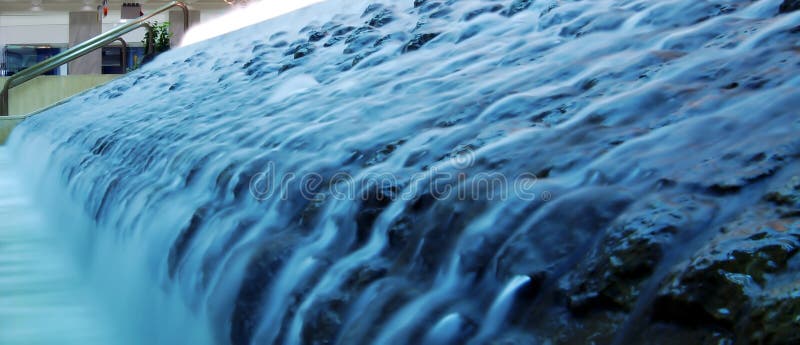 A man-made waterfall fountain panoramic inside a building with flowing waters blurred due to motion. Man made waterfall stock images, royalty-free photos and pictures