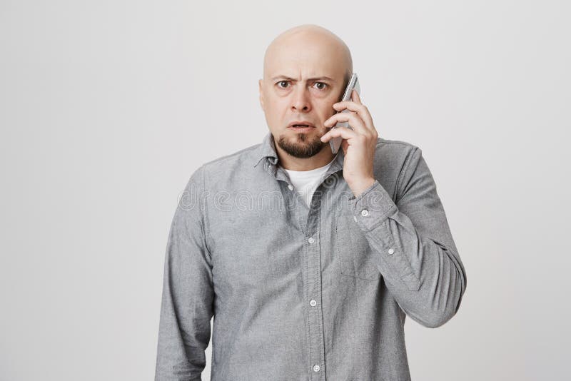 Indoor portrait of worried and confused bald man with beard, talking on phone and being shocked with what he hears royalty free stock image Indoor portrait of worried and confused bald man with beard, talking on phone and being shocked with what he hears royalty free stock image