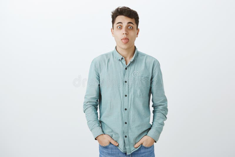 Indoor shot of carefree funny caucasian male in turquois casual shirt, holding hands in pockets, staring at camera and stock photo Indoor shot of carefree funny caucasian male in turquois casual shirt, holding hands in pockets, staring at camera and stock photo