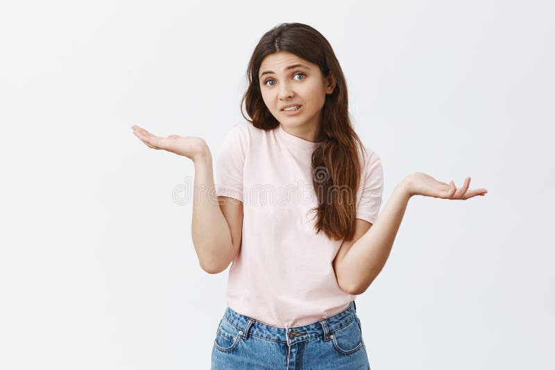 Indoor shot of confused and unsure attractive european female brunette in stylish pink t-shirt shrugging with hands