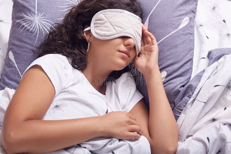 Indoor shot of young beautiful woman sleeping in bed with eye mask, having rest, relaxing during weekend, lying in bed, brunette