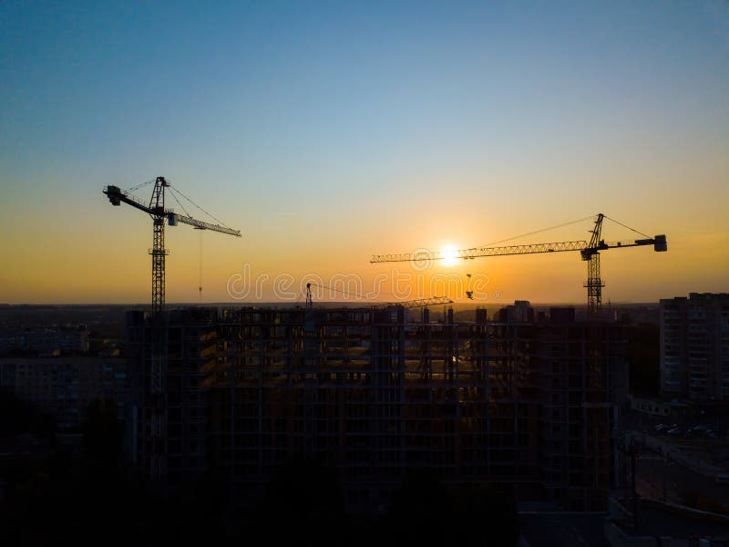 Industrial construction cranes and building silhouettes over sun at sunrise