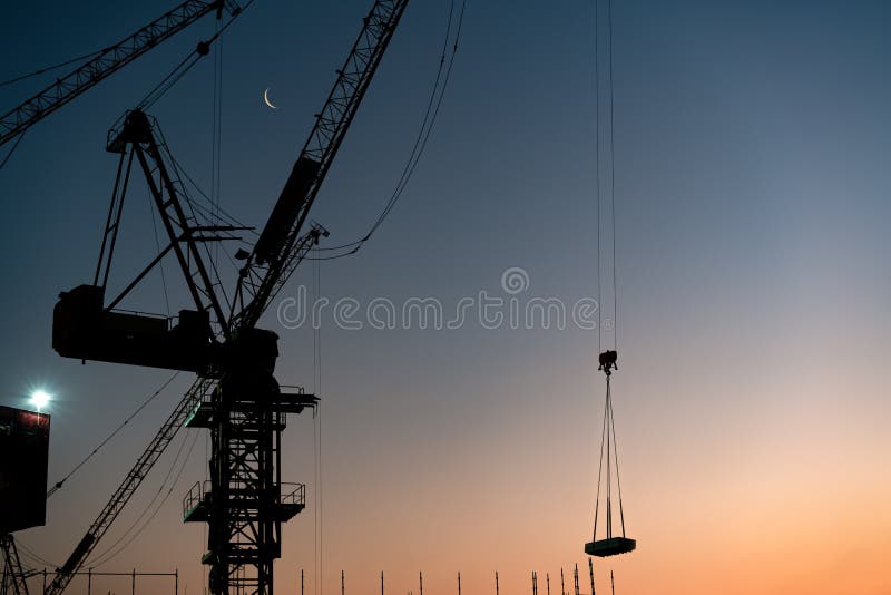 Industrial construction tower crane towering over city and lifting building materials in the afternoon sun stock photography Industrial construction tower crane towering over city and lifting building materials in the afternoon sun stock photography