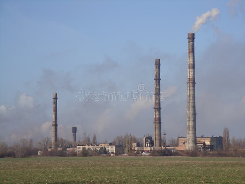 Industrial factory with three smoking pipes in smog clubs. blue sky