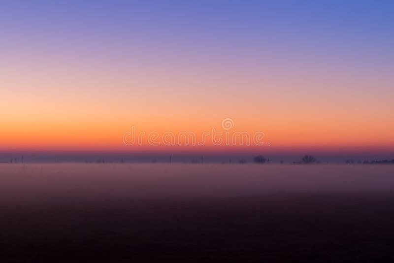 Industrial foggy landscape, silhouette of old factory against the sunset sky and the mist at blue hour at night
