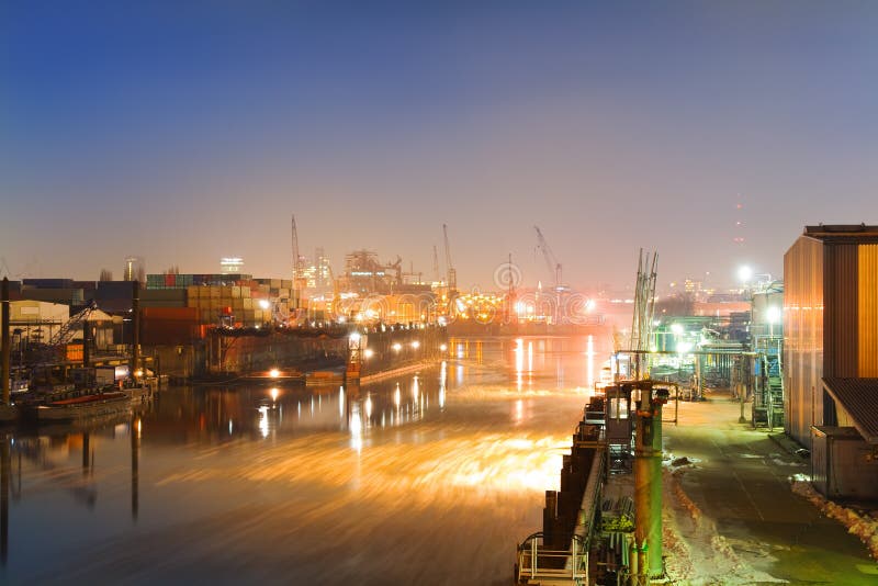Industrial harbor of Hamburg, Germany at night with ships, containers a ship yard as well as cranes and buildings. The sky is clear and blue and the water of the side arm of the river Elbe covered with ice floes. Industrial lights stock images, royalty-free photos and pictures