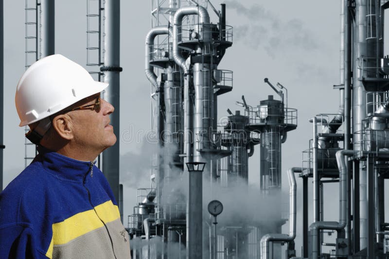 Engineer in hard-hat in foreground, large oil and fuel-refinery in background, blue toning concept. Engineer in hard-hat in foreground, large oil and fuel-refinery in background, blue toning concept