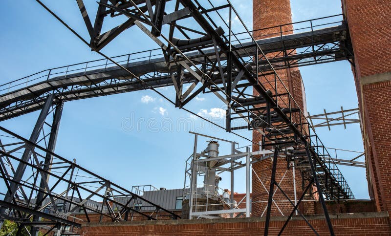 An outside industrial conveyer belt at an old tobacco factory with bright blue sky and a brick smoke tower.