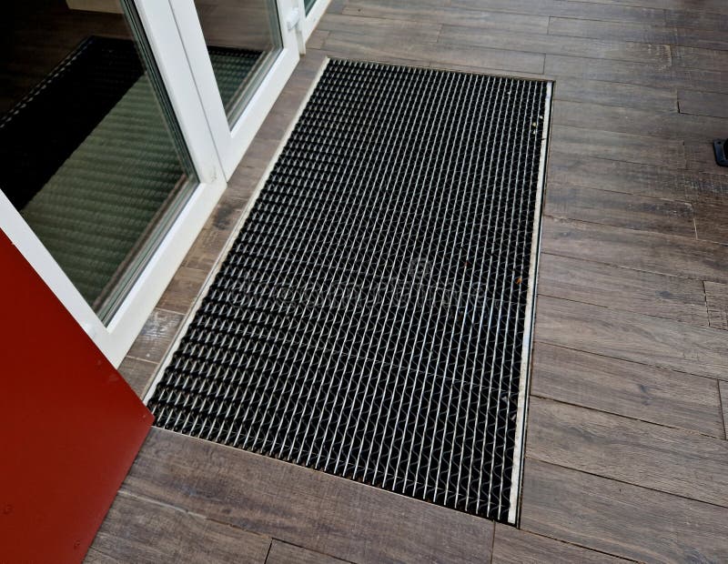 industrial mat cleaning zones at the entrance to the building. A black plastic-metal mat in the shape of an arch or half-circle lies on the limestone gray brown tiles