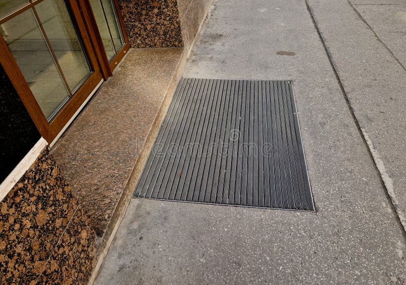 industrial mat cleaning zones at the entrance to the building. A black plastic-metal mat in the shape of an arch or half-circle lies on the limestone mosaic tiles