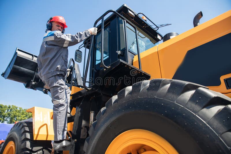 Industrial portrait of working man, excavator driver climbs into cab to perform work on construction site