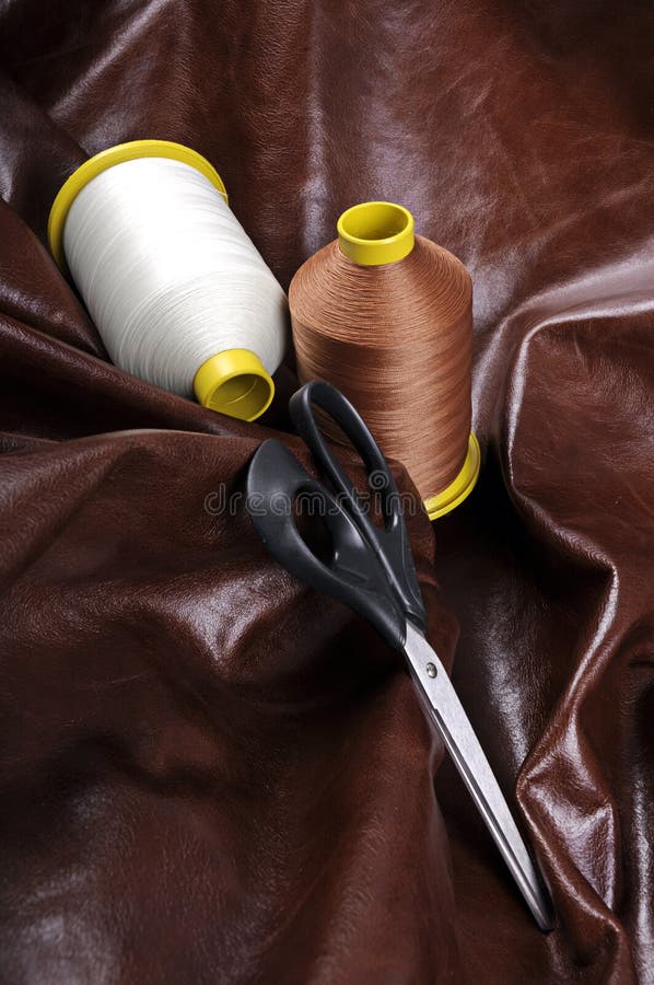 Industrial thread bobbins with scissor on a real leather background