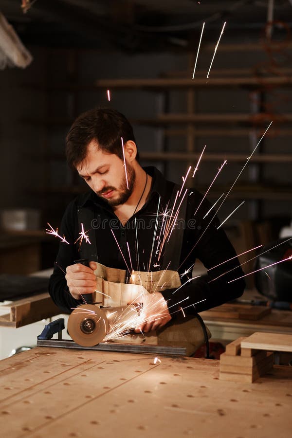 Industrielle Tischlerarbeitskraft, die Metall mit vielen scharfen Funken an einer Werkbank in einer Zimmereiwerkstatt schneidet A stockfoto Industrielle Tischlerarbeitskraft, die Metall mit vielen scharfen Funken an einer Werkbank in einer Zimmereiwerkstatt schneidet A stockfoto
