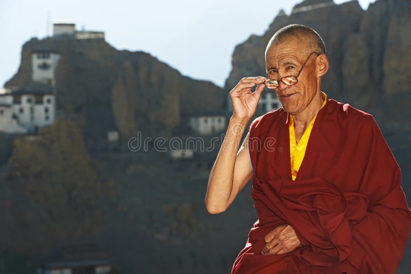 Indian tibetan old monk in red color clothing with glasses in front of monastery. Indian tibetan old monk in red color clothing with glasses in front of monastery