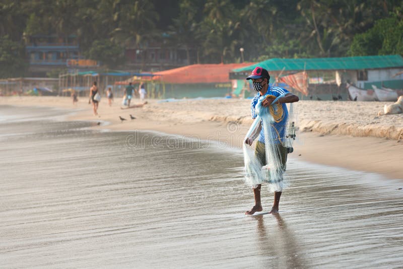 India, GOA, Arambol, fisherman nets fish on the seashore in a protective mask so as not to spread the COVID-19 coronavirus during 21 day quarantine in India, concept of lockdown and curfew. India, GOA, Arambol, fisherman nets fish on the seashore in a protective mask so as not to spread the COVID-19 coronavirus during 21 day quarantine in India, concept of lockdown and curfew