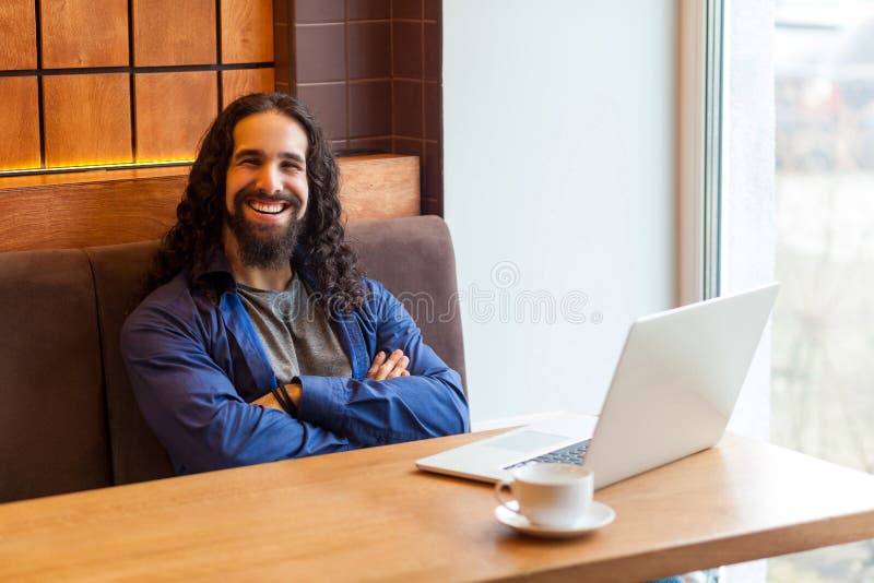 Indépendant barbu bel satisfait de jeune homme dans le style occasionnel se reposant en café avec l'ordinateur portable, les bras image libre de droits Indépendant barbu bel satisfait de jeune homme dans le style occasionnel se reposant en café avec l'ordinateur portable, les bras image libre de droits