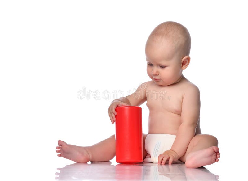 Infant child baby boy in diaper is sitting on the floor looking on a red cylinder in front of him, playing, touching royalty free stock photography Infant child baby boy in diaper is sitting on the floor looking on a red cylinder in front of him, playing, touching royalty free stock photography