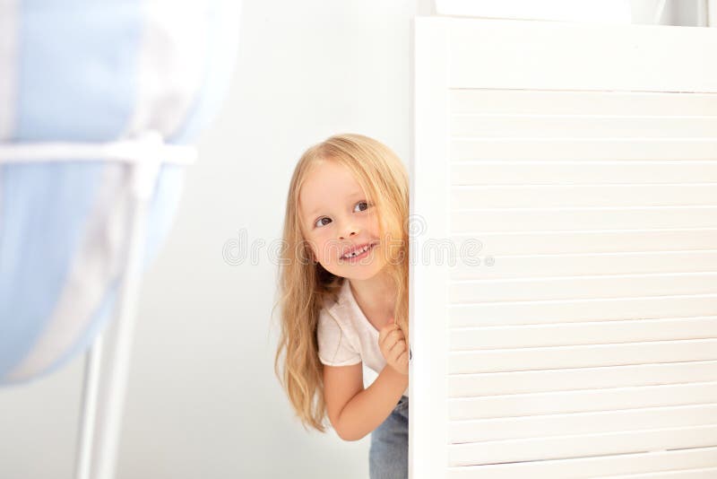 Infanzia, divertimento e concetto di gente - Bello e felice bambina sorridente nascosta dietro la porta della stanza Il bambino g