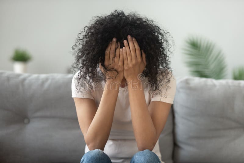 Infeliz mujer afroamericana sosteniendo la cabeza en las manos llorando imagen de archivo