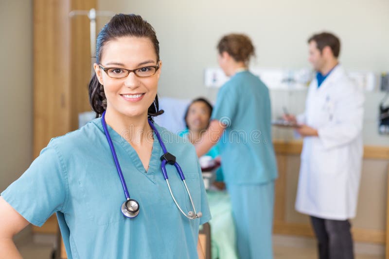 Infermiere Smiling Against Patient e Team In medico fotografia stock libera da diritti Infermiere Smiling Against Patient e Team In medico fotografia stock libera da diritti