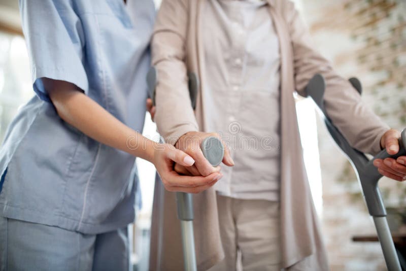 Infirmière portant l'uniforme soutenant une femme avec des béquilles images libres de droits