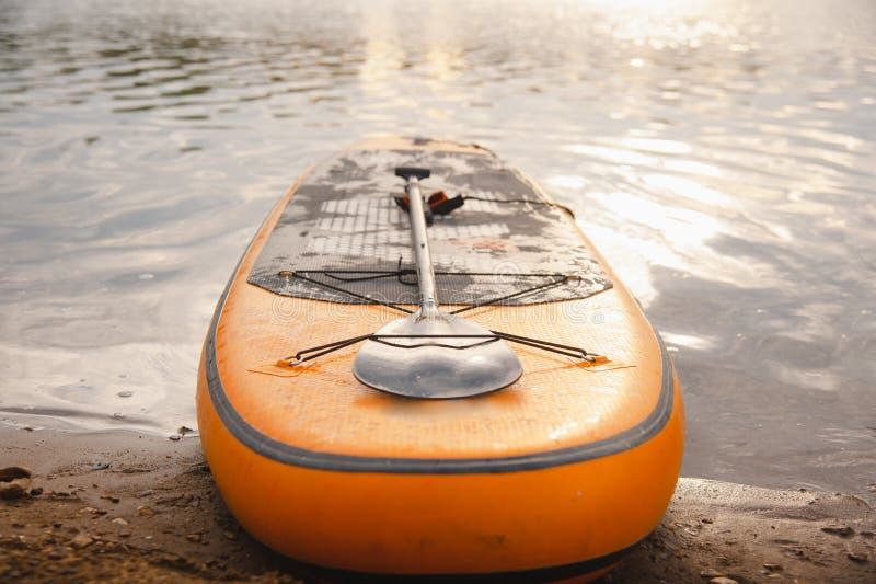 An inflatable SUP board with an orange paddle lies on the beach. Surfboard on the beach royalty free stock images