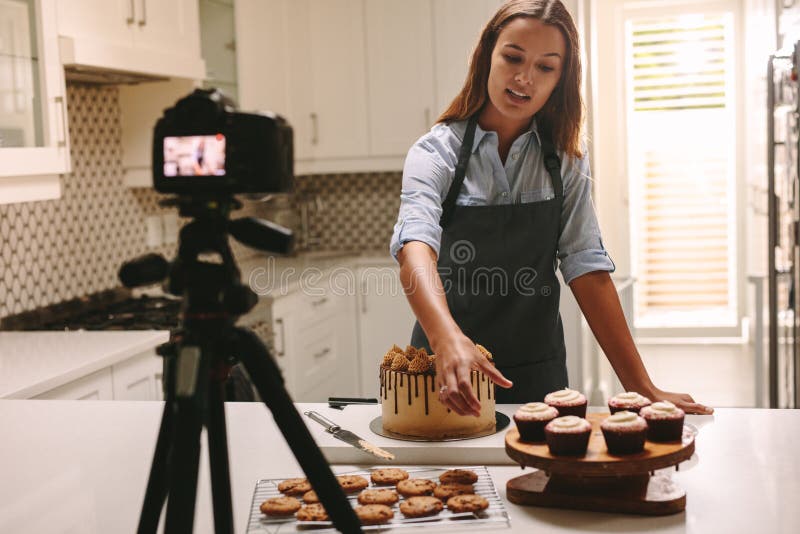Social media influencer woman recording video content in kitchen, showing confectionery on table. Female confectioner filming herself of her online culinary show. Social media influencer woman recording video content in kitchen, showing confectionery on table. Female confectioner filming herself of her online culinary show