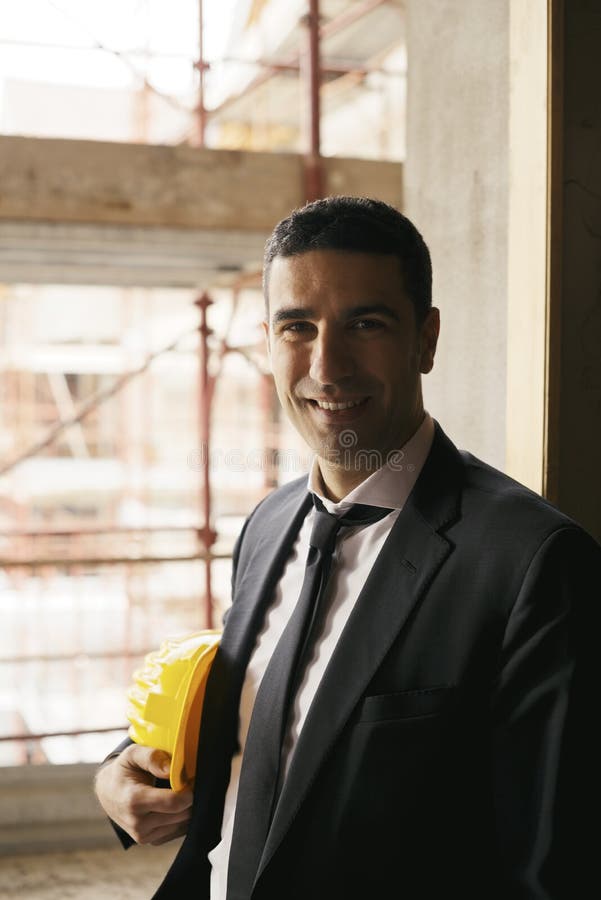 Ingeniero con el casco en emplazamiento de la obra que sonríe en la cámara, por fotos de archivo libres de regalías Ingeniero con el casco en emplazamiento de la obra que sonríe en la cámara, por fotos de archivo libres de regalías