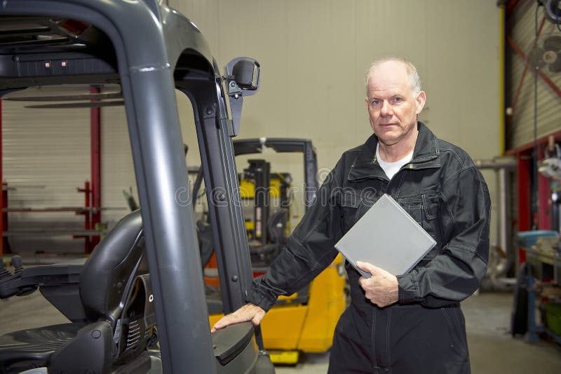 Forklift maintenance engineer holding the manual, ready with his after sales inspection in a workshop dealier and garage. Forklift maintenance engineer holding the manual, ready with his after sales inspection in a workshop dealier and garage