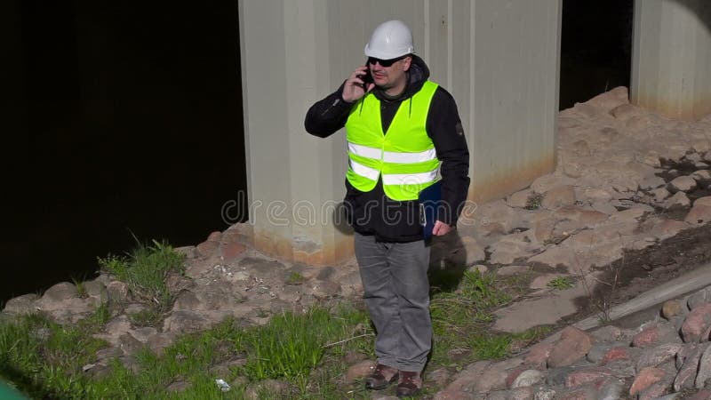 Ingenieur, der am intelligenten Telefon nahe Brückenbau spricht stock footage