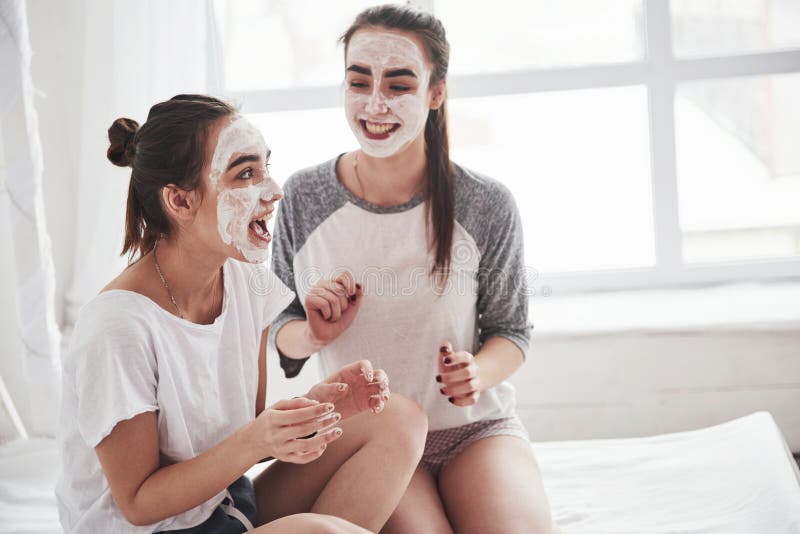Inget behov av spa-salong Beaktande av hudvård genom användning av vit mask på ansiktet Två kvinnliga systrar har helg i sovrumme fotografering för bildbyråer Inget behov av spa-salong Beaktande av hudvård genom användning av vit mask på ansiktet Två kvinnliga systrar har helg i sovrumme fotografering för bildbyråer