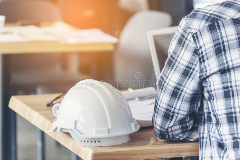 Inginer constructor civil care lucrează cu notebook-ul la birou, cu hard disk de siguranță alb-gălbui la birou pe șantierul de con royalty free stock images