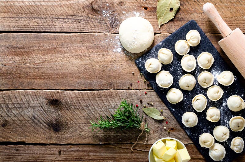 Ingredienser för framställning av pelmenien, ravioli, klimpar - deg, rosmarin, kavel, kanfastråd, smör, lagerblad överkant arkivfoton