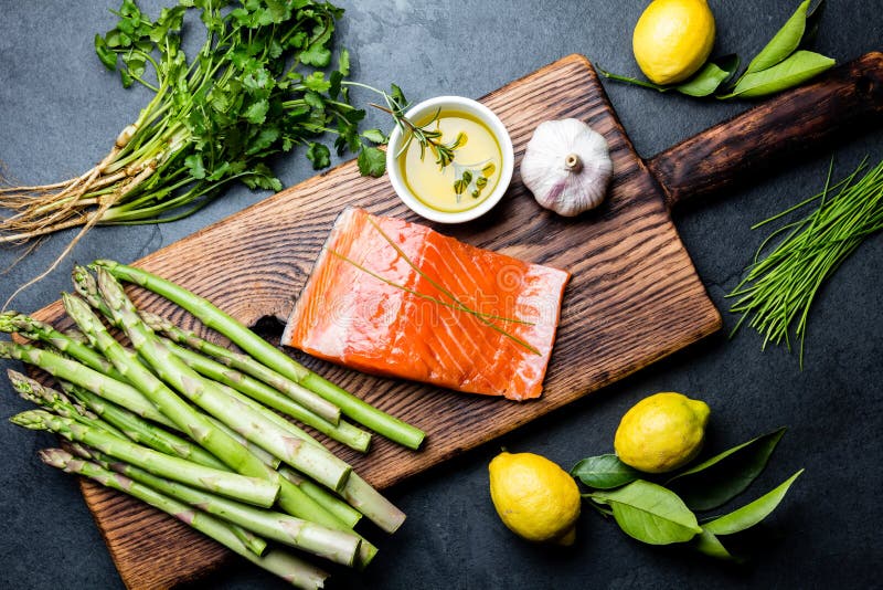 Ingredienser för matlagning Rå laxfilé, sparris och örter på träbräde Matmatlagningbakgrund med kopieringsutrymme royaltyfri foto