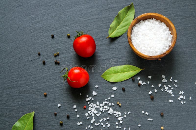 Ingredientes alimentarios: tomates, hojas del laurel de bahía y sal en piedra negra de la pizarra Visión superior fotografía de archivo libre de regalías Ingredientes alimentarios: tomates, hojas del laurel de bahía y sal en piedra negra de la pizarra Visión superior fotografía de archivo libre de regalías