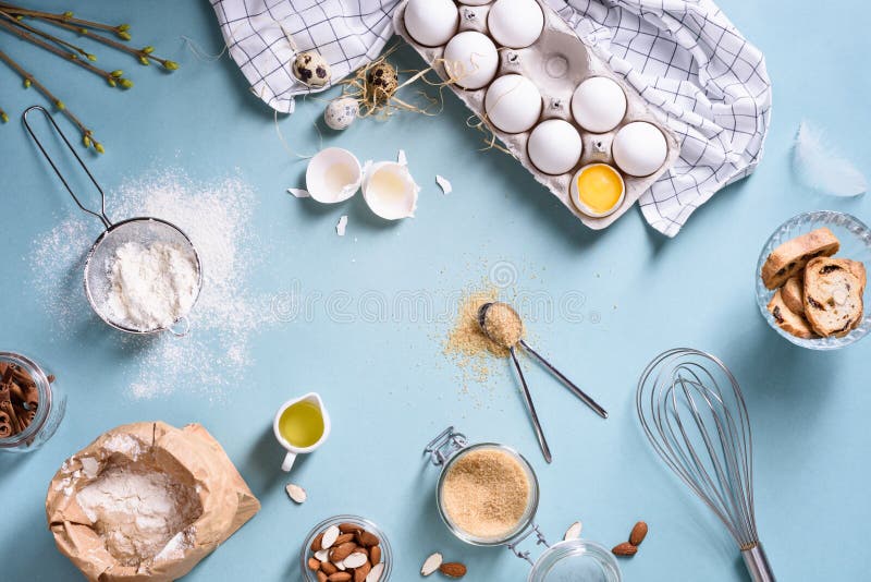 Ingredientes da padaria - farinha, ovos, manteiga, açúcar, gema, porcas da amêndoa na tabela azul Conceito doce do cozimento da p